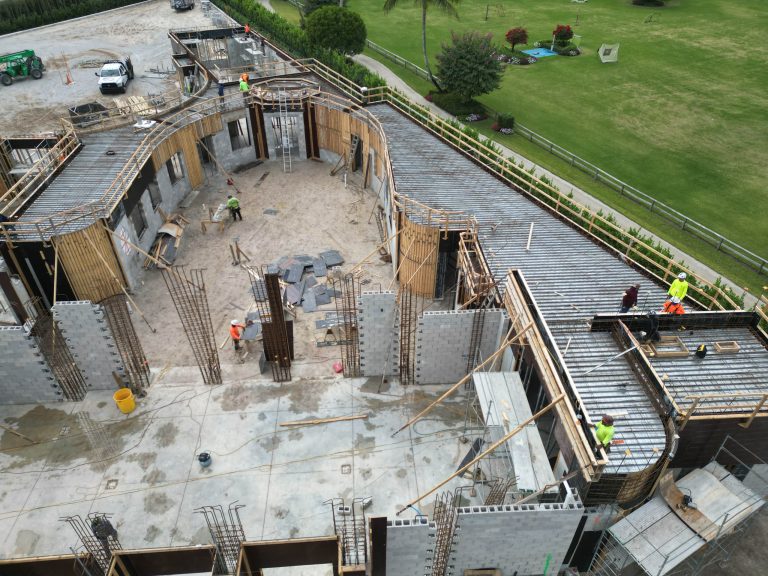 Aerial view of a building under construction on an Equestrian Estate in Wellington. Workers in safety gear navigate concrete walls, metal reinforcements, and wooden scaffolding as tools and materials scatter across the unfinished floor.