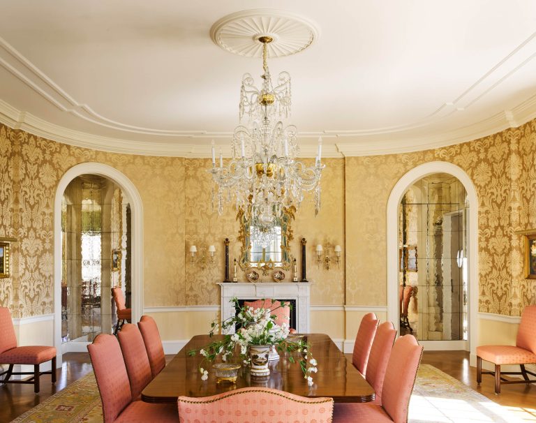 Elegant dining room with arched doorways, a crystal chandelier, ornate gold wallpaper, and a polished wood table surrounded by pink-upholstered chairs. This Fifth Avenue Renovation captures classic New York sophistication in every detail.