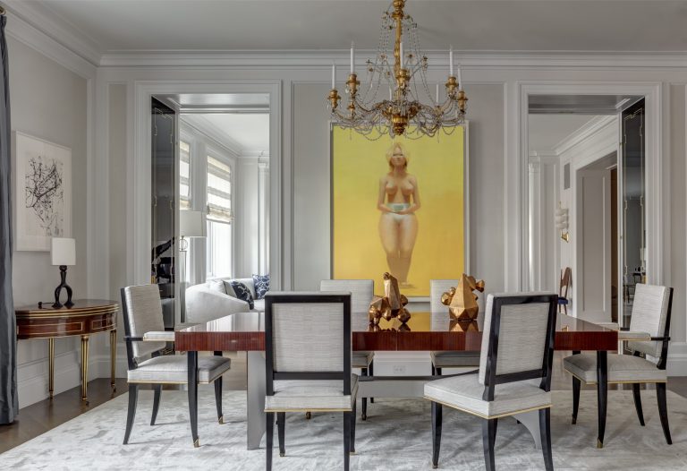 A formal Park Ave Apartment dining room in New York features six upholstered chairs around a rectangular wooden table, a large chandelier above, and a striking painting of a nude woman with a yellow background. Large mirrors and decorative accents complete the elegant decor.