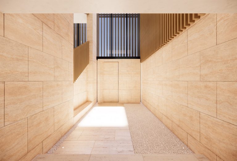 A minimalist corridor with light beige stone walls and floor, a section of white pebbles on the right, and wooden slats on the upper right and in front of a window above a closed door at the end. Sunlight streams in, creating a bright, clean atmosphere.